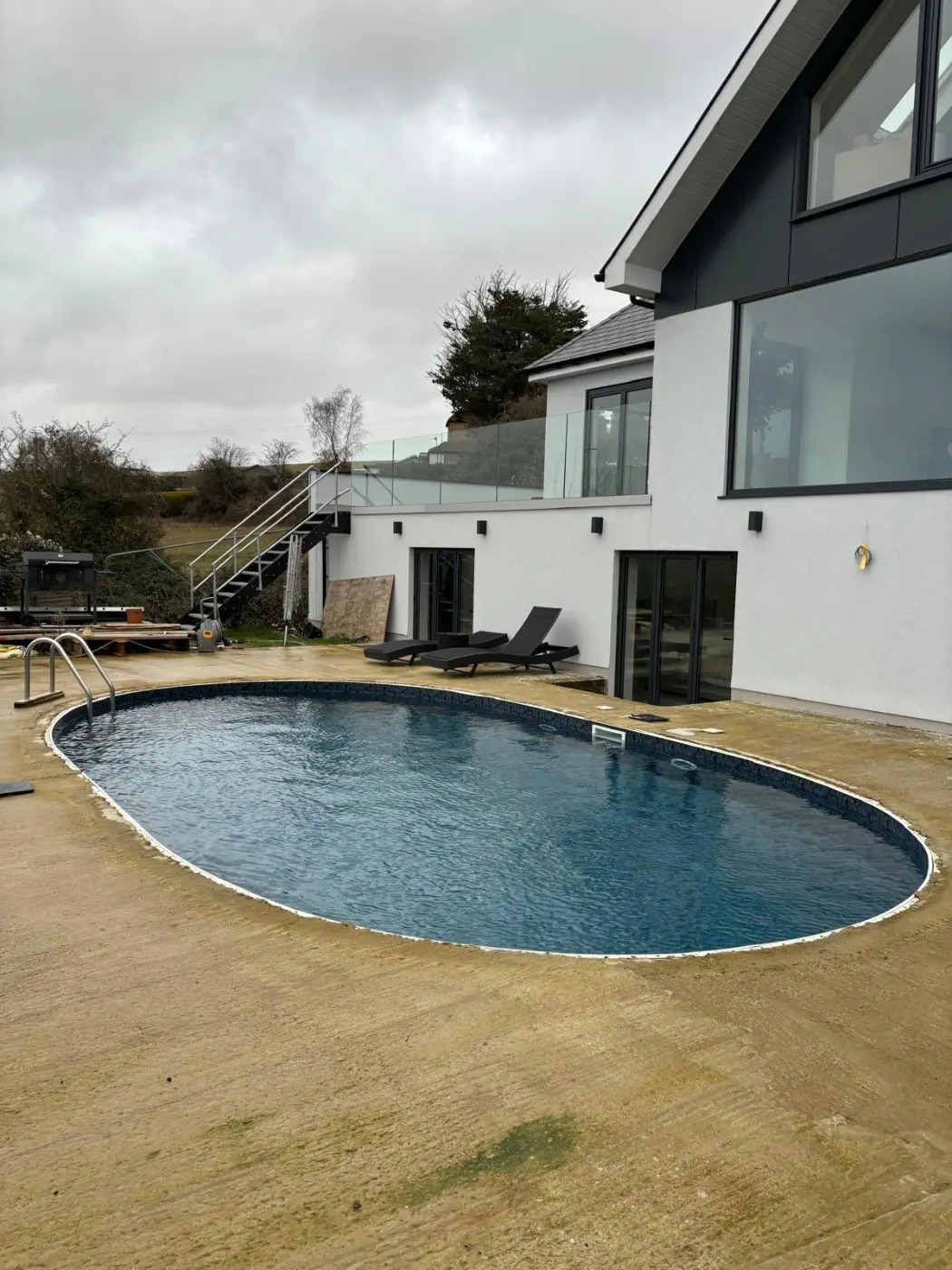 Completed hillside house overlooking a curved swimming pool